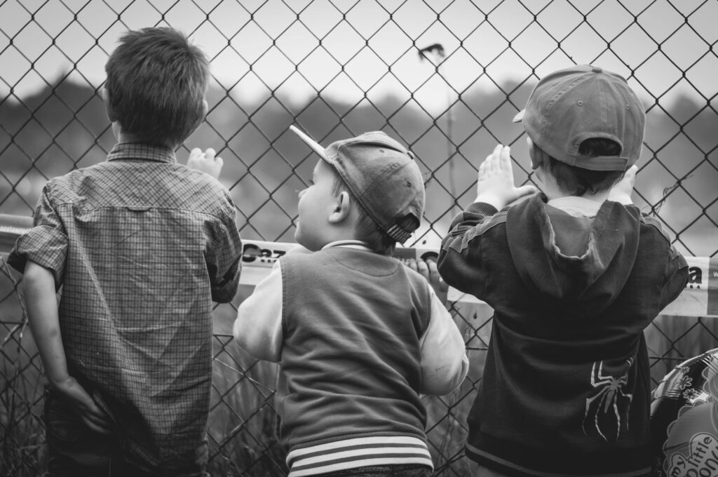 Black and white image of three young boys peering through a chain-link fence.